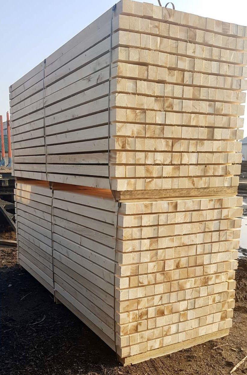 Stos belek drewnianych o przekroju kwadratowym, ułożonych warstwami na paletach, zabezpieczonych taśmą, widoczne słoje drewna.