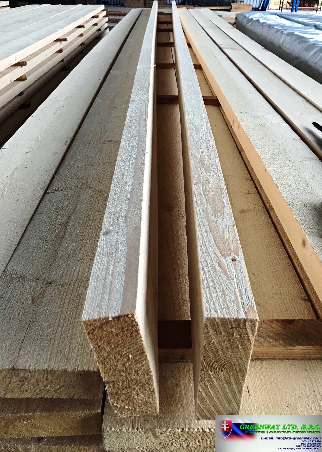 Stos surowych, jasnych desek i kantówek z widocznym przekrojem drewna, ułożonych warstwami na magazynie, z logo firmy Greenway Ltd w prawym dolnym rogu.