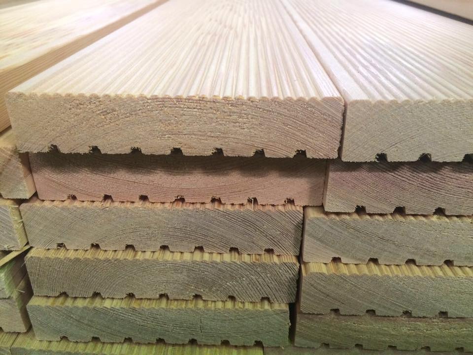 Stos desek tarasowych z drewna iglastego, widoczne rowki wentylacyjne i struktura drewna.