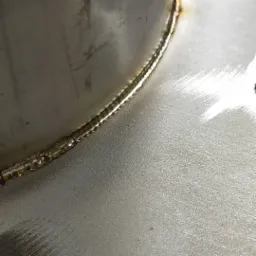 Szczegółowy widok spoiny TIG na nierdzewnej rurze, ukazujący precyzyjne łączenie i delikatną strukturę powierzchni metalu.