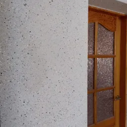 Ściana wewnętrzna pokryta białą, dekoracyjną strukturą z czarnymi i srebrnymi drobinkami, sąsiadująca z drewnianymi drzwiami z szybą o fakturze szkła ornamentowego.