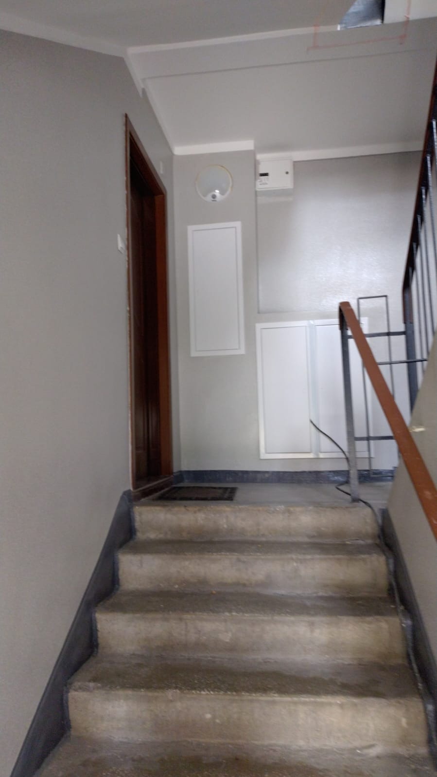 Klatka schodowa w bloku po malowaniu ścian na szaro, widoczne schody z szorstką fakturą, drzwi wejściowe i poręcze schodów.