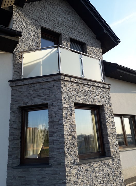 Nowoczesny balkon z balustradą ze szkła mlecznego i nierdzewnej stali na elewacji z szarego kamienia łupanego.