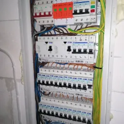 Rozdzielnica elektryczna z zainstalowanymi bezpiecznikami, przewodami i listwami zaciskowymi wewnątrz obudowy, widoczne różne modele i marki zabezpieczeń.