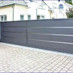 Nowoczesna, przesuwna brama w kolorze grafitowym z poziomymi, srebrnymi akcentami, zamontowana przed domem z jasną elewacją i brukowanym podjazdem.