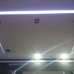 Nowoczesny sufit podwieszany z oświetleniem LED i punktowymi lampami w łazience z ciemnymi płytkami.