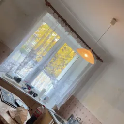 Wnętrze kuchni w trakcie remontu, widoczne niedomalowane ściany, stara kuchenka, okno z widokiem na drzewa z ż&oacute;łtymi liśćmi, butelka napoju na stole.