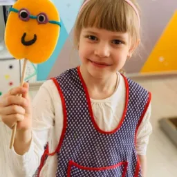 Dziewczynka z Łasku trzyma ręcznie robioną kukiełkę z gąbki z uśmiechem i okularami, prawdopodobnie wykonaną podczas warsztatów animacyjnych.