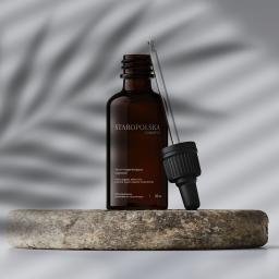 Czyste Formy - Butelka brązowego serum Staropolska Cosmetics z pipetą, umieszczona na szorstkim kamieniu na tle z cieniem liścia palmy.