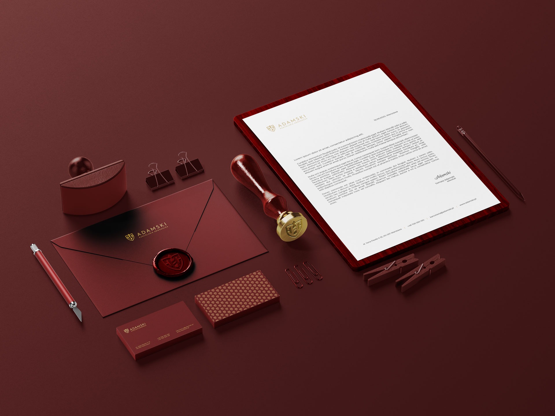 Zestaw papeterii firmowej w odcieniach bordo z elementami złota, zawierający list, kopertę z pieczęcią, wizytówki, ołówek i akcesoria biurowe, prezentujący elegancki branding kancelarii adwokackiej.