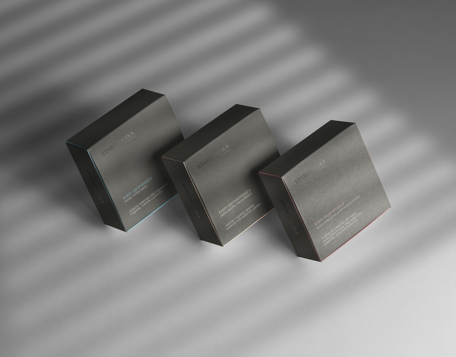 Trzy pudełka kosmetyków marki Staropolska Cosmetics w odcieniach szarości, z różnymi rodzajami kremów: ujędrniającym, wzmacniającym i regenerującym, ustawione pod kątem na szarym tle z cieniami.