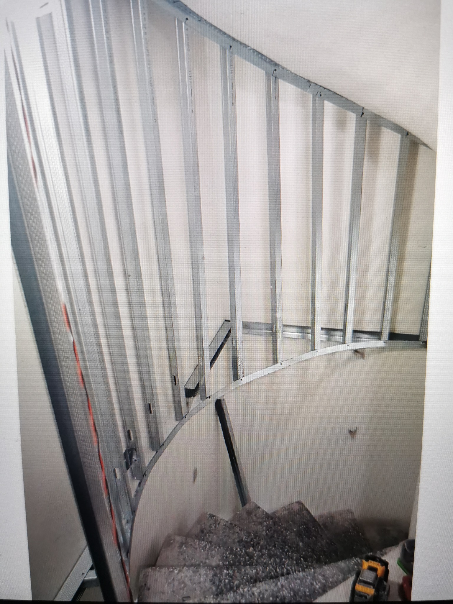 Metalowa konstrukcja szkieletowa pod zabudowę na zakrzywionej ścianie przy schodach, widoczne zabawki na schodach.