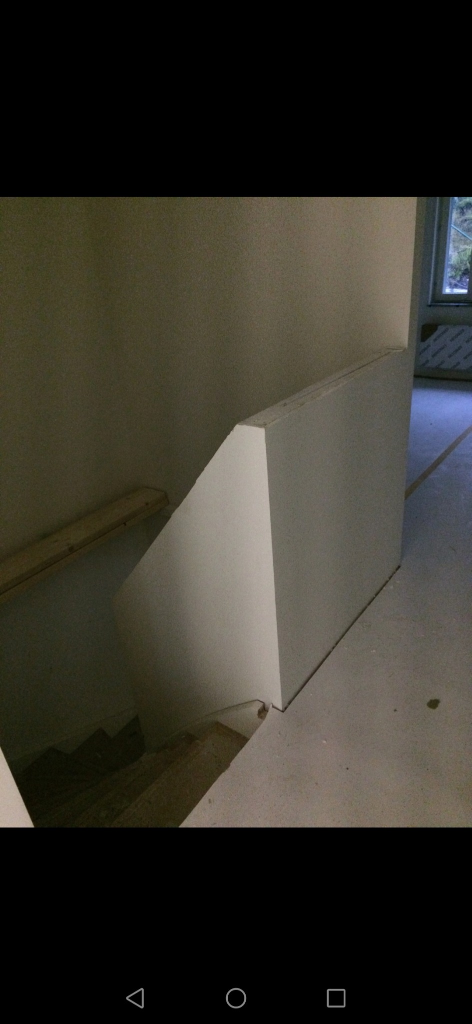 Niedokończona zabudowa schodów przy użyciu białych płyt, widoczne drewniane elementy konstrukcyjne i surowy beton na podłodze.