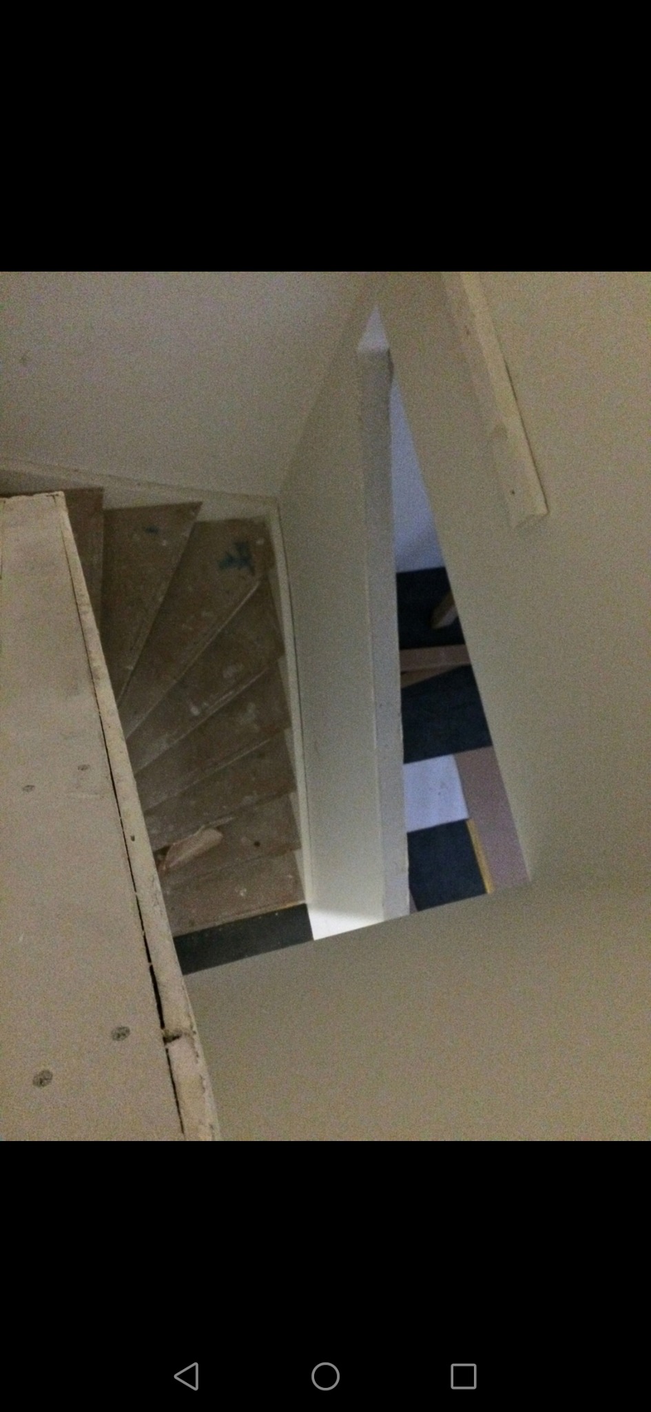 Widok z góry na schody w trakcie remontu, z widoczną płytą karton-gips na ścianie i podłogą z czarno-białymi płytkami w tle.