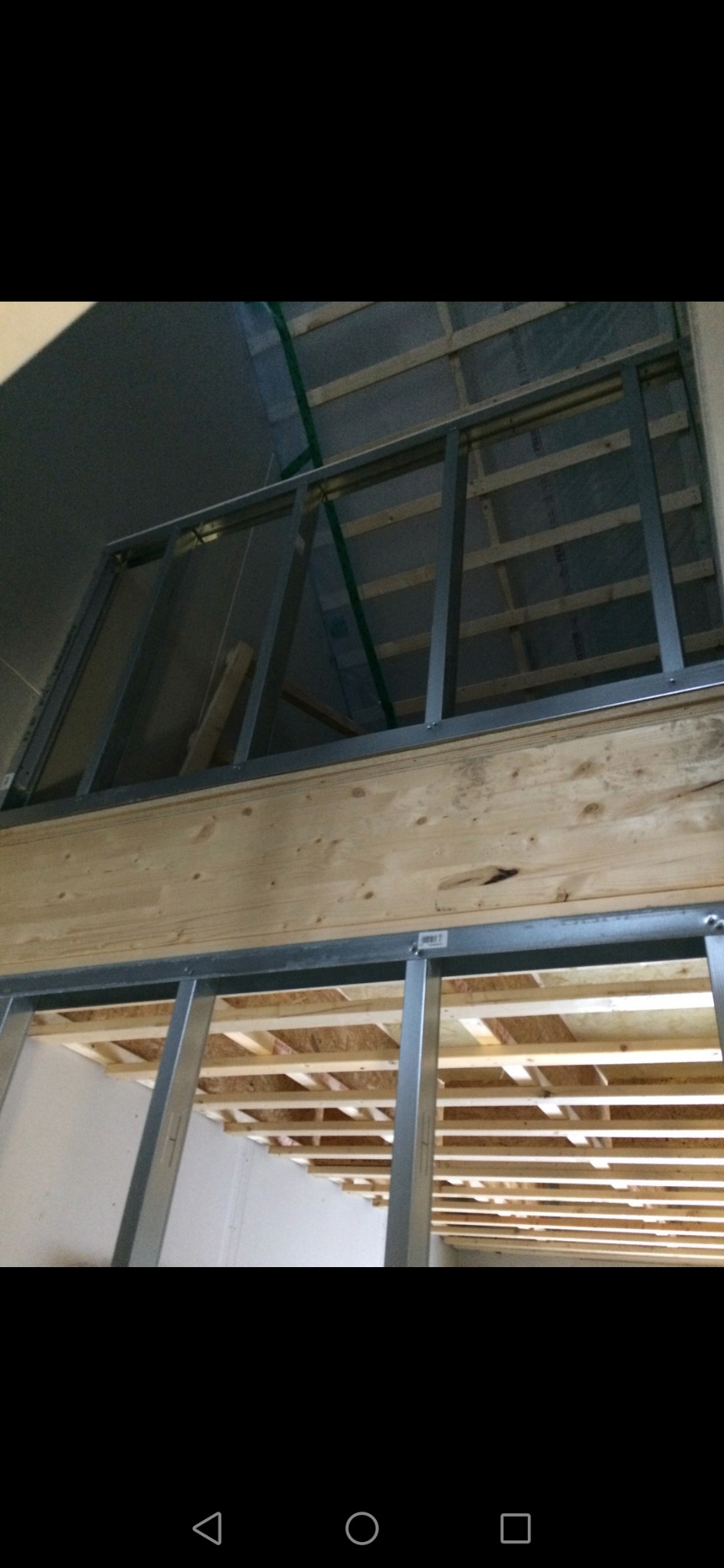 Stelaż z metalowych profili wewnątrz budynku, widoczne drewniane elementy konstrukcyjne stropu i ściany, przygotowanie do montażu okładzin.