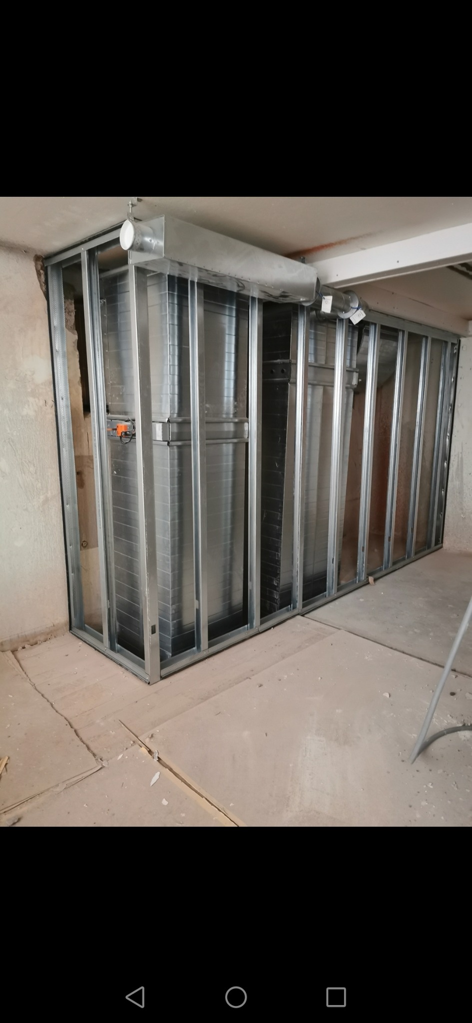 Metalowa konstrukcja szkieletowa ścianki działowej z widocznymi profilami i elementami mocującymi, surowy stan podłogi, fragment instalacji wentylacyjnej pod sufitem.