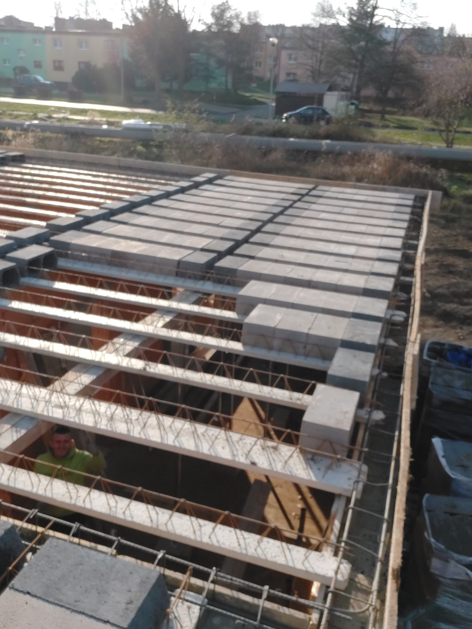 Budowa stropu Teriva: widok na ułożone bloczki betonowe na belkach stalowych, z widocznym pracownikiem w tle i elementami zbrojenia oraz deskowania.