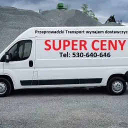 Biały samochód dostawczy z napisem 'SUPER CENY' i numerem telefonu na tle hałdy żwiru.