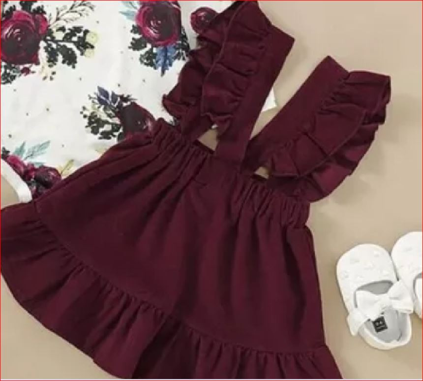 Komplet niemowlęcy: bordowa sukienka na szelkach z falbankami i bluzka w kwiaty, obok białe buciki.