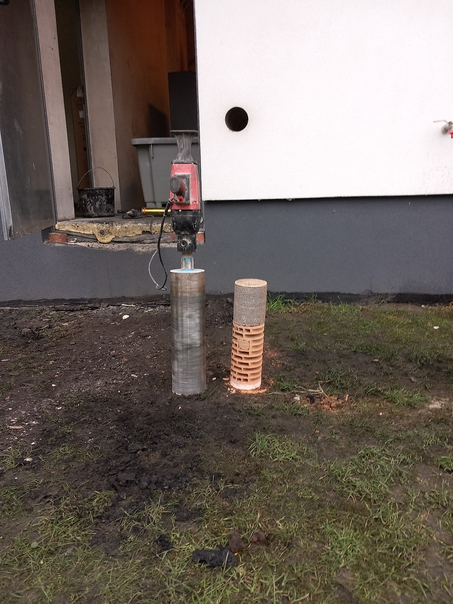 Wiertnica diamentowa z wyciętym rdzeniem betonowym i ceglanym przed białą ścianą budynku z widocznym otworem.