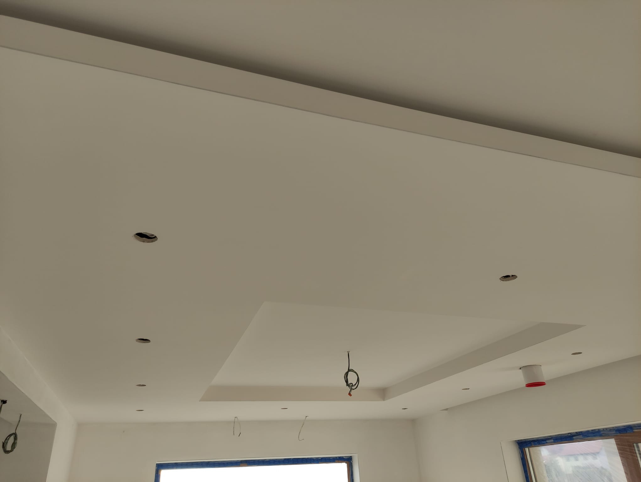 Wnętrze w Wołominie w trakcie prac wykończeniowych: widok na sufit podwieszany z wyciętymi otworami na oświetlenie, widoczne kable elektryczne i elementy konstrukcyjne.