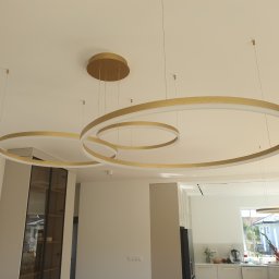 Jarosław Florkiewicz - Nowoczesne oświetlenie: trzy złote, okrągłe lampy wiszące na cienkich linkach w jasnym wnętrzu. Minimalistyczny design z elementami złota.