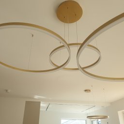 Jarosław Florkiewicz - Nowoczesne oświetlenie sufitowe: złote, okrągłe lampy wiszące tworzą unikalny wzór na białym suficie. Minimalistyczny design wnętrza.