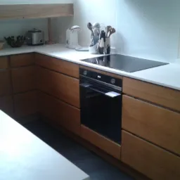 Nowoczesna kuchnia z drewnianymi frontami szafek, białym blatem i zabudowaną płytą indukcyjną oraz piekarnikiem w Mielcu. Na blacie widoczne akcesoria kuchenne i toster.