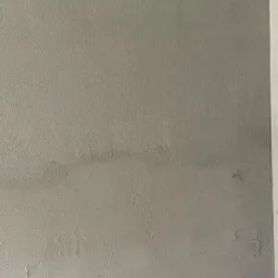 Świeżo nałożona, szara warstwa tynku na ścianie wewnętrznej, widoczne delikatne nierówności i ślady po narzędziach, przygotowana do dalszej obróbki.