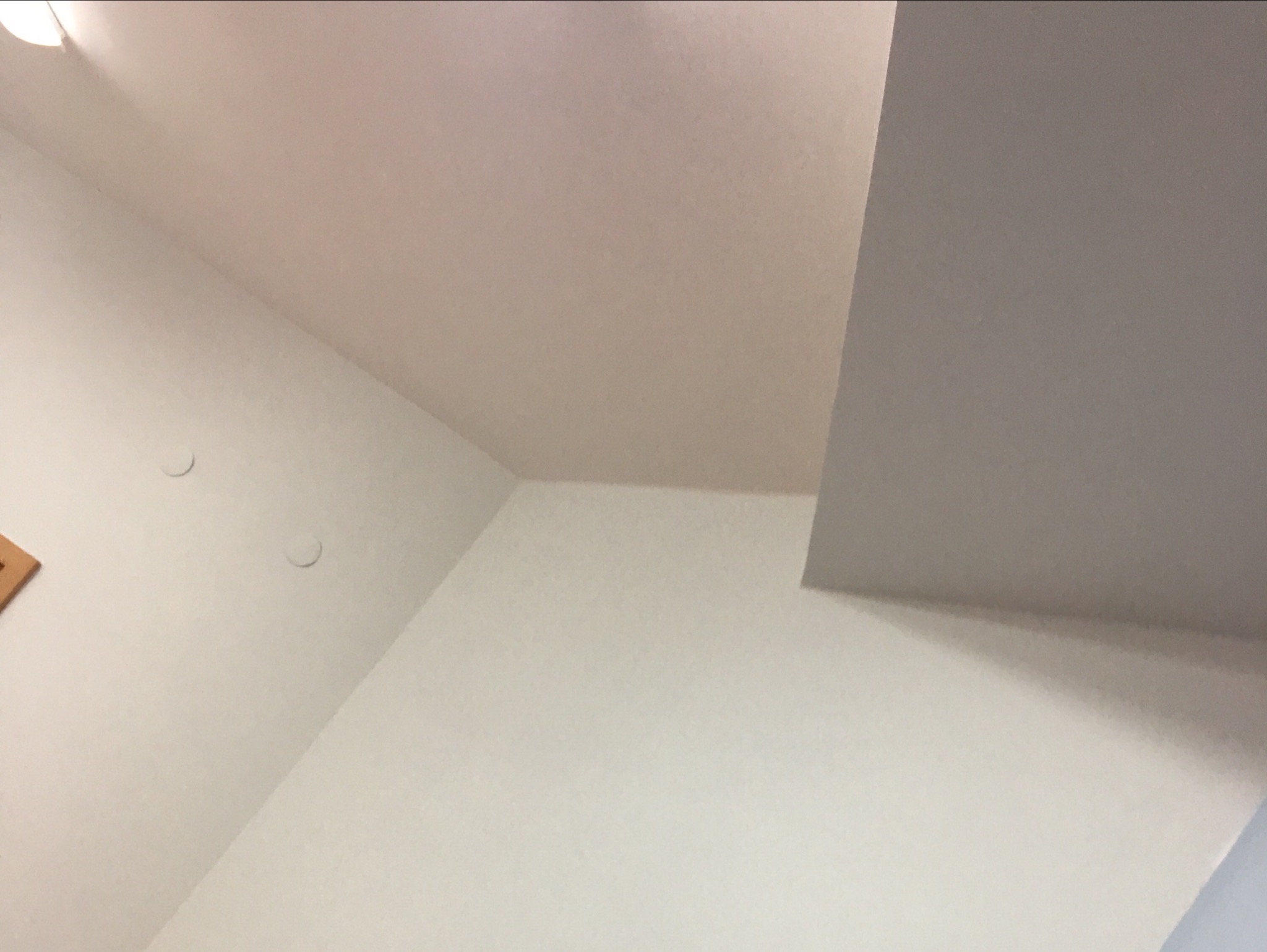 Skośny sufit i ściany w jasnym, neutralnym kolorze, widoczne dwa okrągłe punkty oświetleniowe oraz fragment ramy obrazu w rogu.