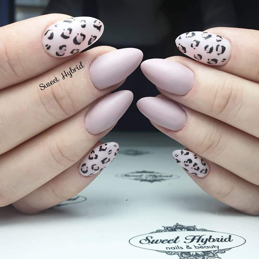 Dłonie prezentują matowe, pudrowo-różowe paznokcie, z akcentami w postaci białych paznokci z czarnym wzorem panterki.