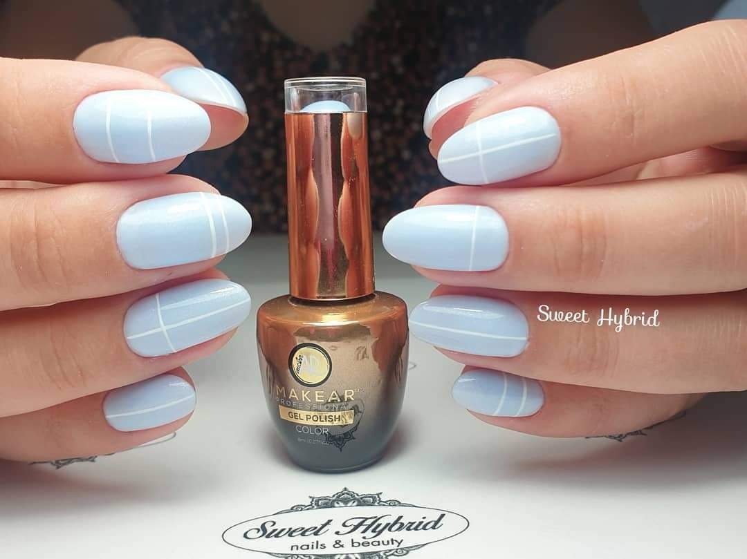 Pastelowe, błękitne paznokcie z białymi liniami, prezentowane obok buteleczki lakieru hybrydowego MakeAr, na białym tle.