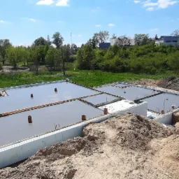 Wylany beton na przygotowany fundament z izolacją termiczną, widok z góry na plac budowy w słoneczny dzień.