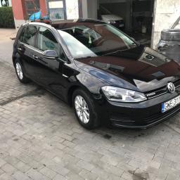 Auto serwis - Błyszczący czarny Volkswagen Golf po umyciu, zaparkowany na kostce brukowej przed warsztatem z widocznymi śladami wody.