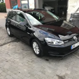 Błyszczący czarny Volkswagen Golf po umyciu, zaparkowany na kostce brukowej przed warsztatem z widocznymi śladami wody.