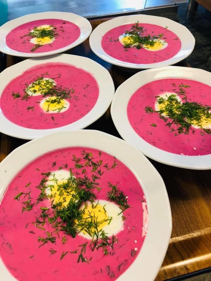 Cztery talerze chłodnika litewskiego z jajkiem i koperkiem, ustawione na drewnianym blacie, widok z góry.