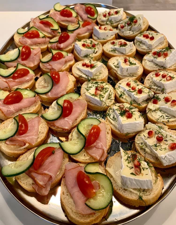 Elegancko ułożone na srebrnej tacy okrągłe kanapeczki: połowa z szynką, ogórkiem i pomidorkiem koktajlowym, druga połowa z serem brie, koperkiem i granatem.