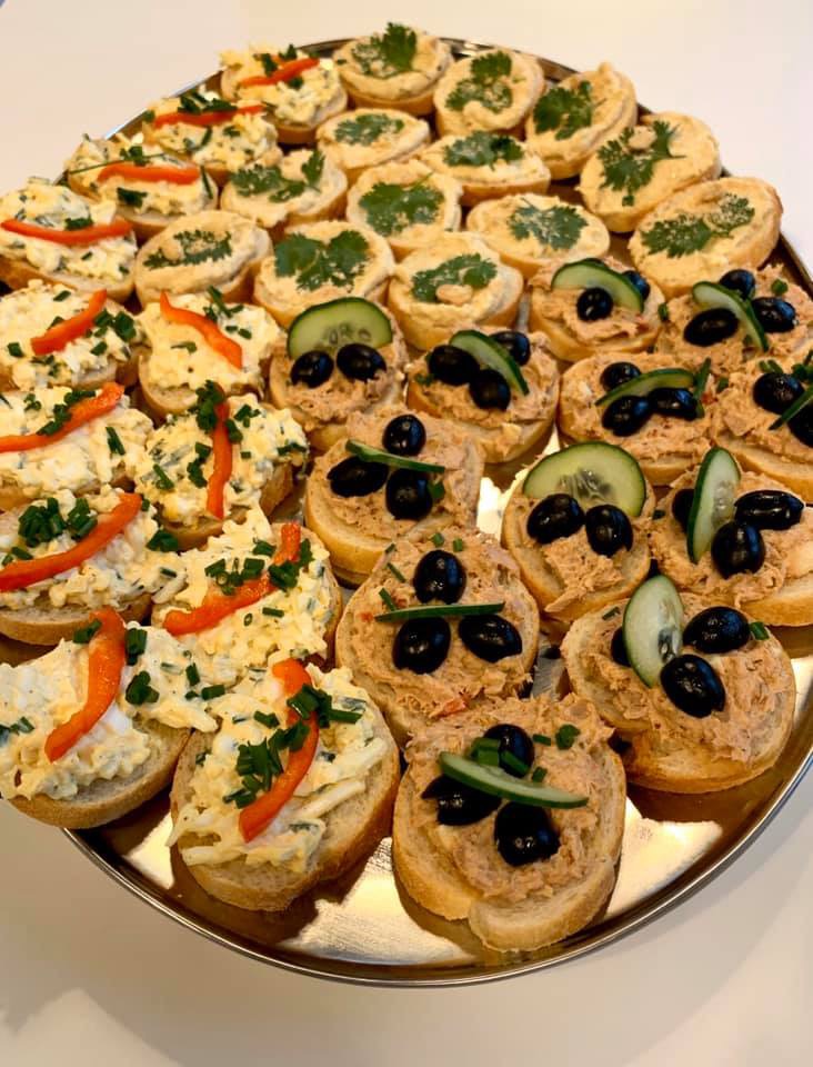 Srebrna taca z różnorodnymi kanapeczkami: z pastą jajeczną i czerwoną papryką, z pastą rybną, oliwkami i ogórkiem oraz z kremowym serkiem i natką pietruszki.