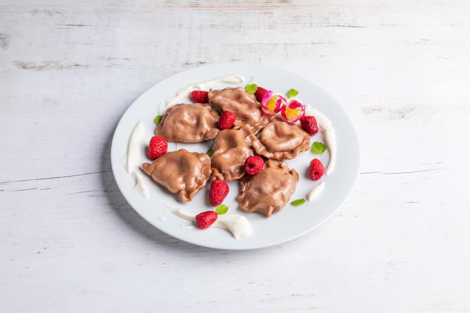 Czekoladowe pierogi z malinami, miętą i kleksami śmietany na białym talerzu, dekorowane tulipanami, na tle białych desek.