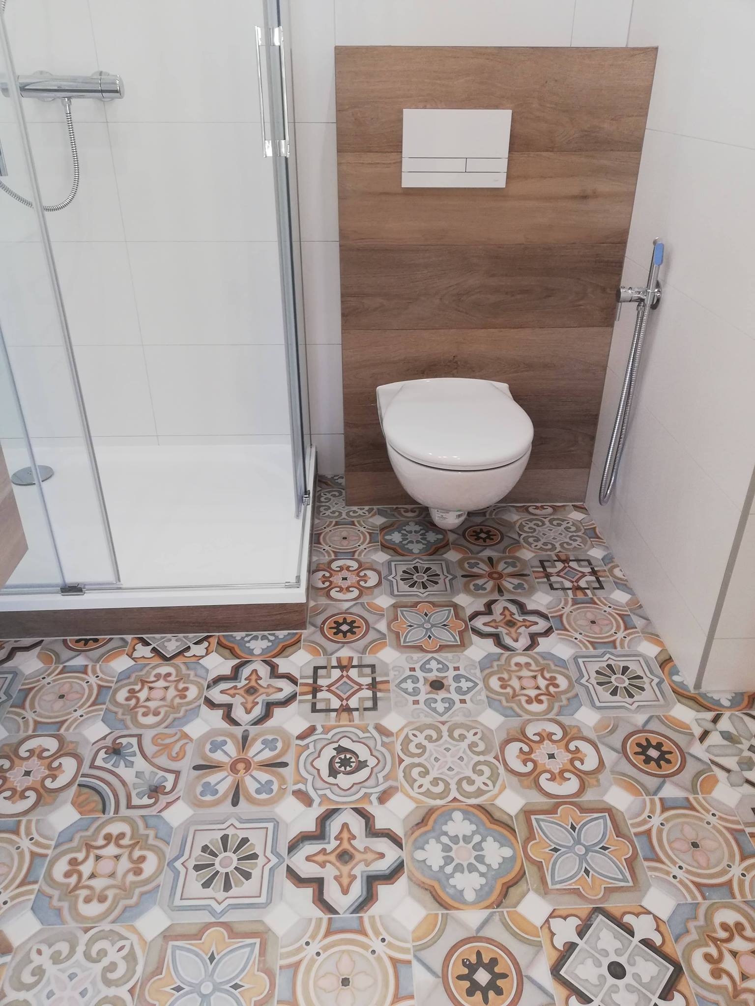 Ukończona łazienka z kabiną prysznicową, podwieszaną toaletą i wzorzystymi płytkami podłogowymi w stylu patchwork.