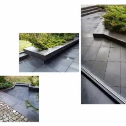 Nowoczesny taras wyłożony ciemnymi płytami, z podwyższonymi rabatami obsadzonymi zielenią, widok z góry przez okno, po deszczu.