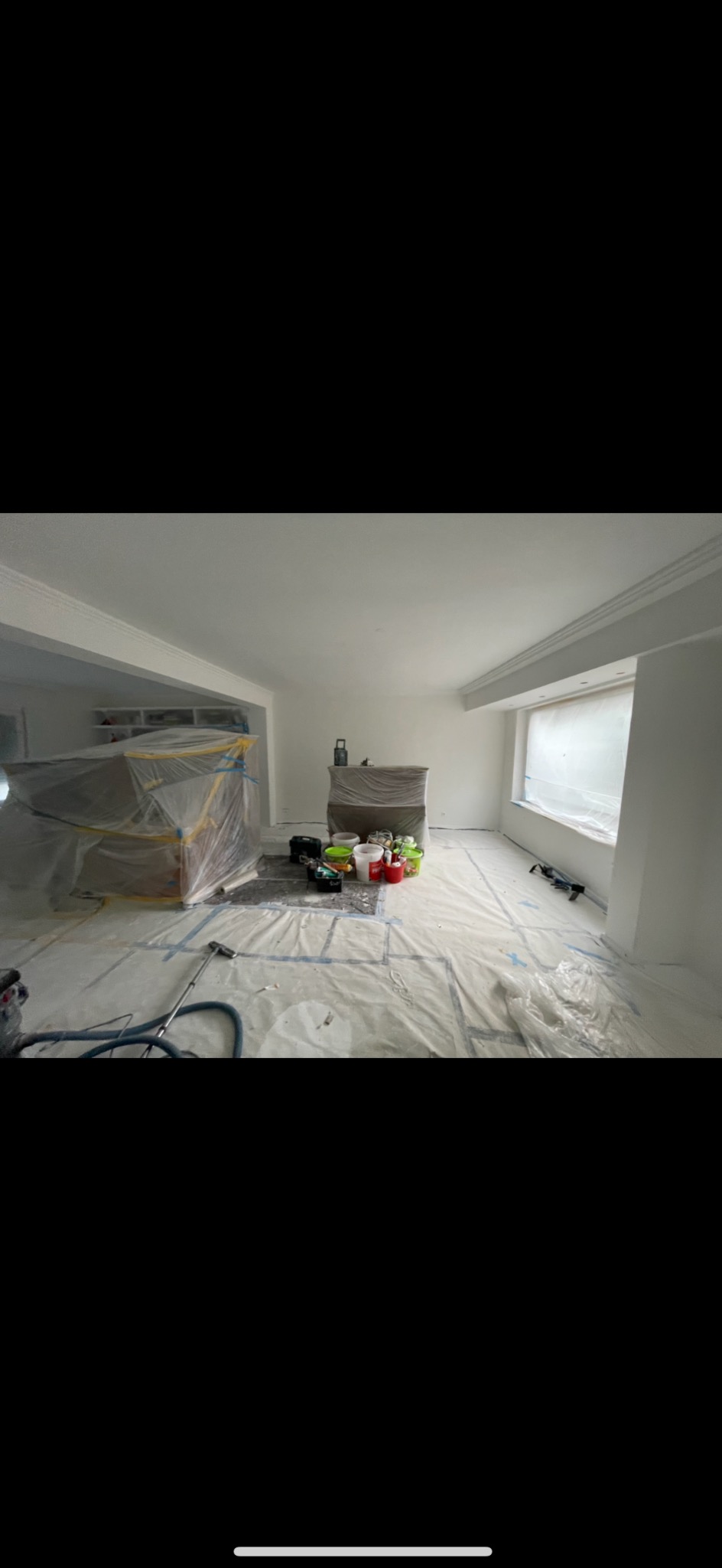 Pokój w trakcie odświeżania: świeżo pomalowane białe ściany, meble zabezpieczone folią malarską, podłoga zakryta folią ochronną, widoczne narzędzia i farby przygotowane do dalszych prac.