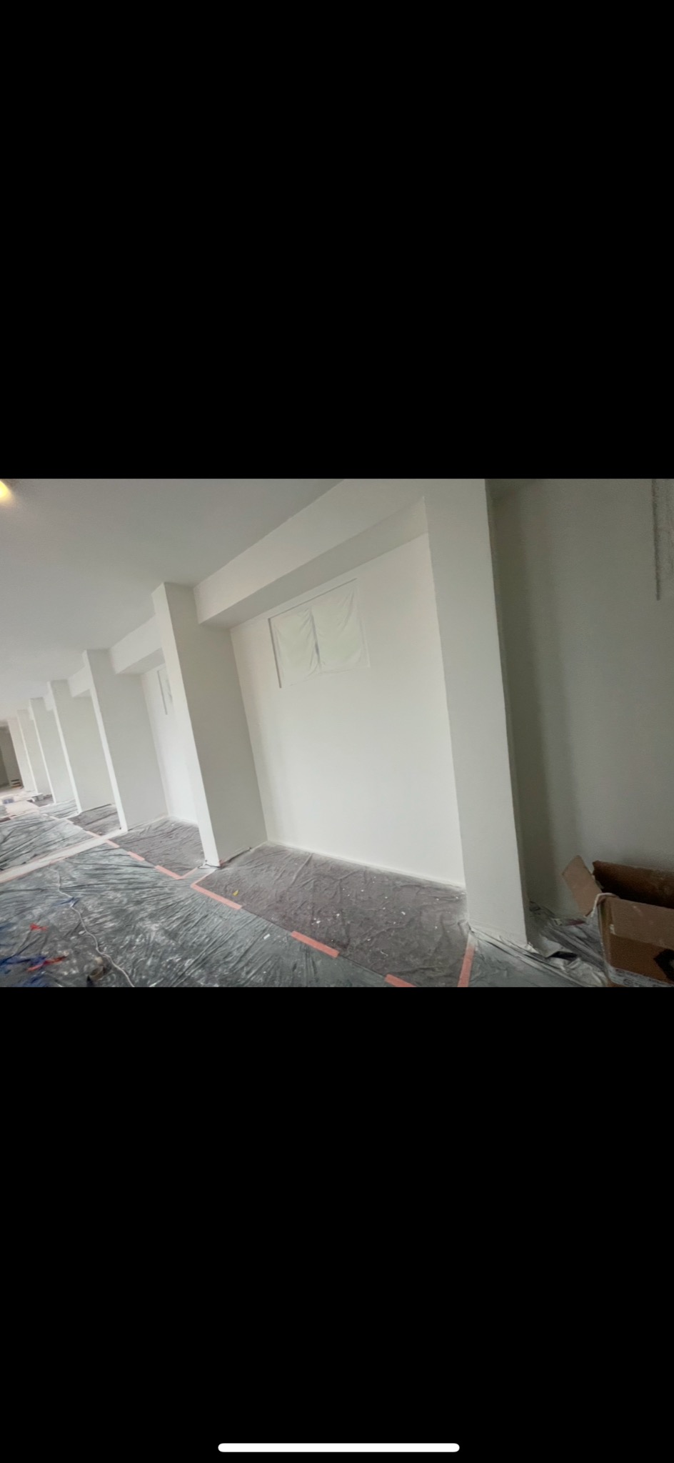 Wnętrze w trakcie odświeżania: świeżo pomalowane białe ściany, podłoga zabezpieczona folią ochronną, widoczne kartony w rogu pomieszczenia.