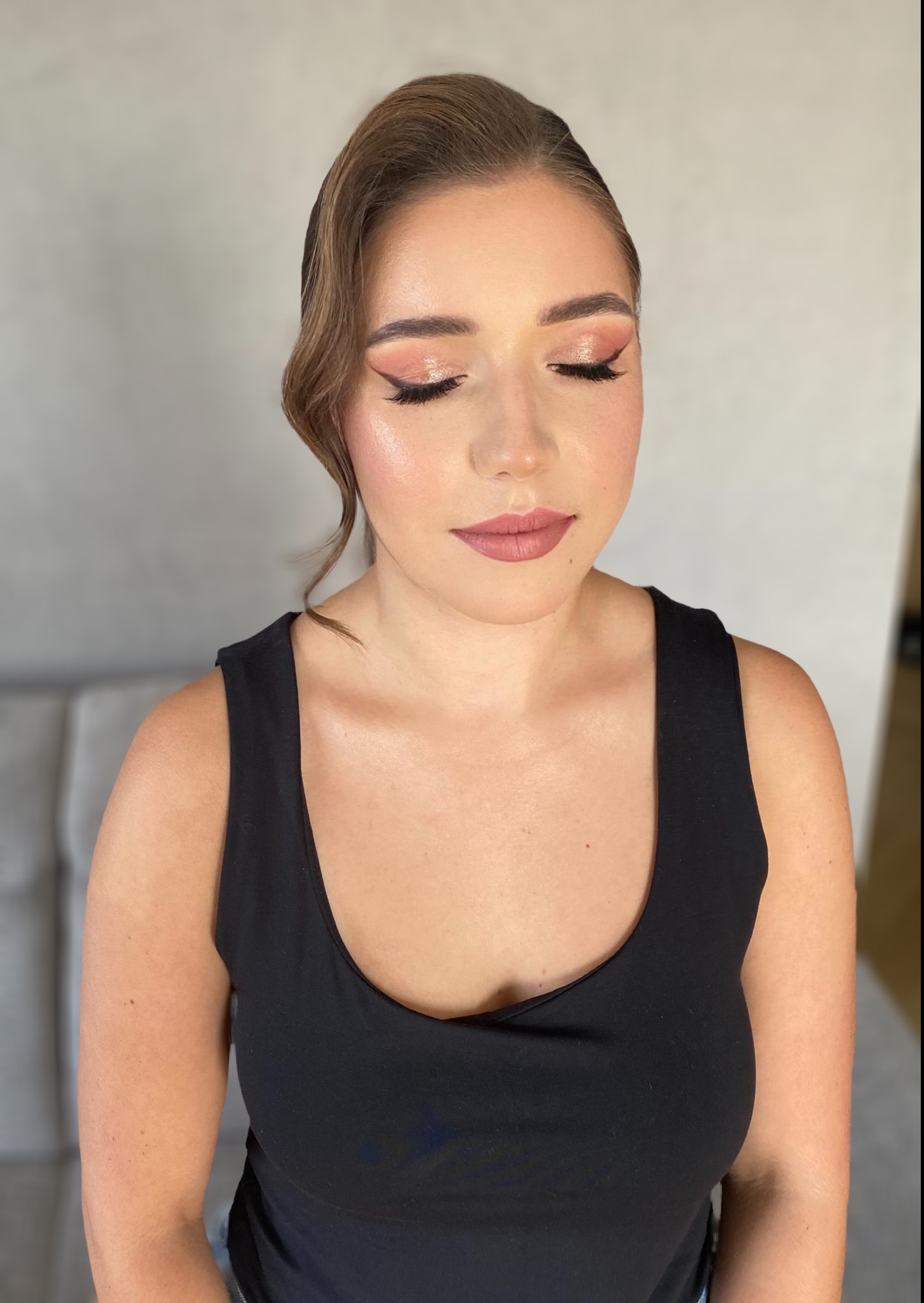 Portret kobiety z zamkniętymi oczami po wykonanym delikatnym, różowym makijażu z eyelinerem i upiętymi włosami w stylu retro.