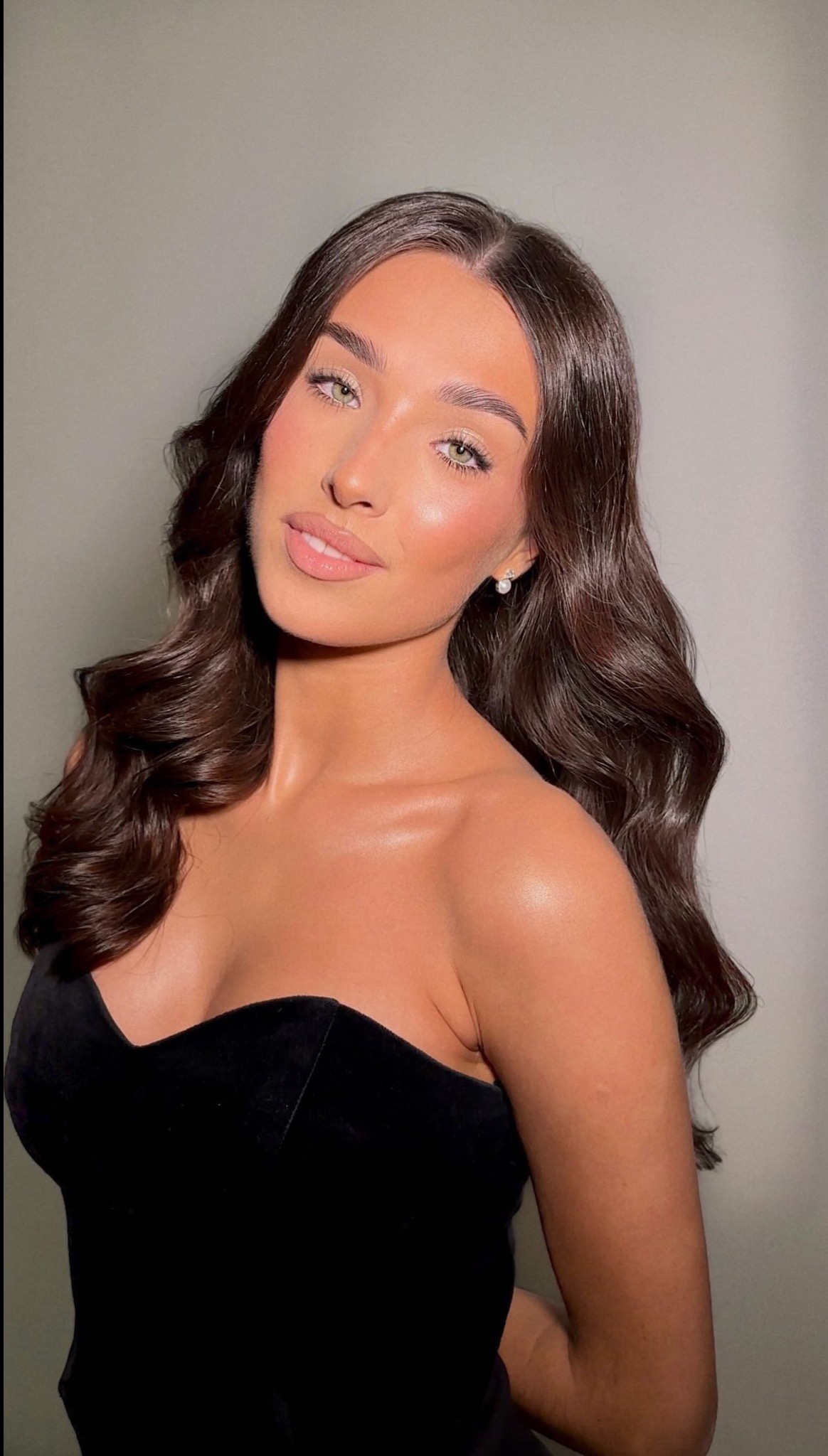 Portret kobiety z profesjonalnie wykonanym konturowaniem, rozświetlaczem i delikatnym różem na policzkach, podkreślonymi zielonymi oczami, pełnymi ustami w jasnym odcieniu i ciemnymi, falującymi...