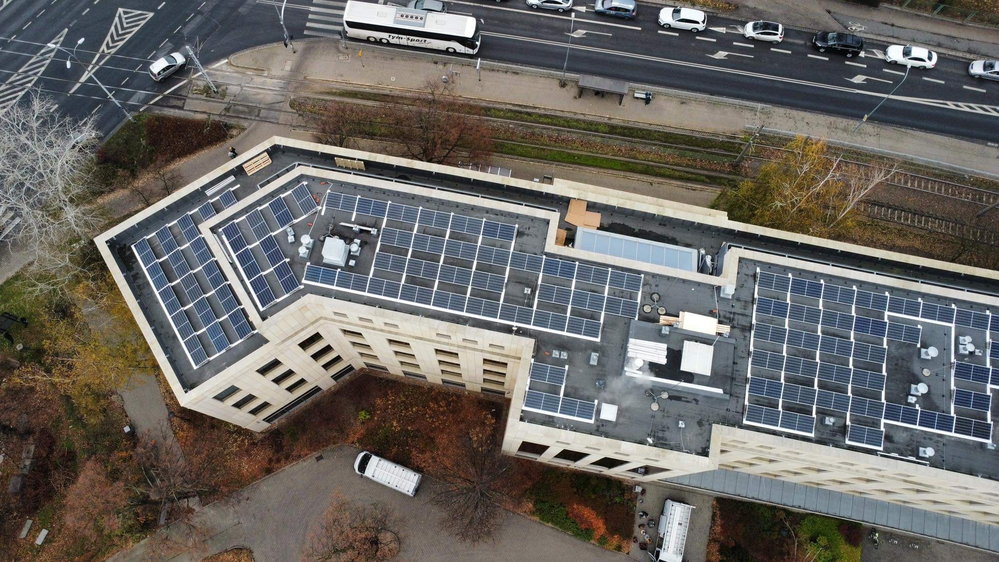 Widok z góry na budynek z zainstalowanymi panelami słonecznymi na dachu, obok torów kolejowych i ulicy z ruchem samochodowym.