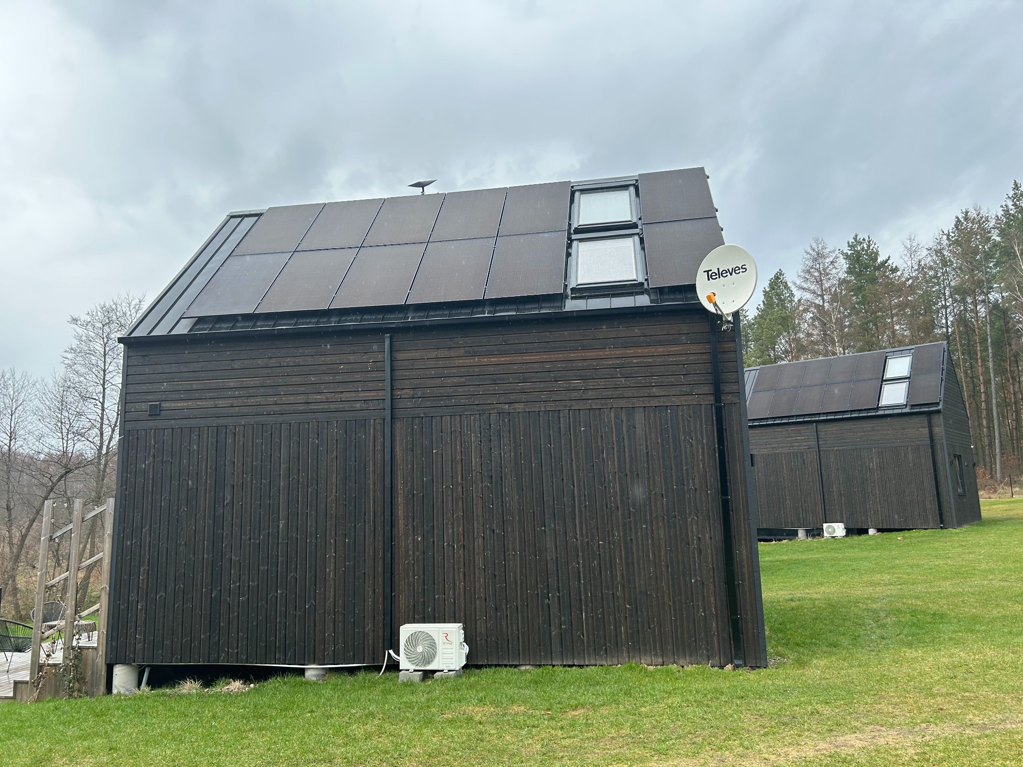 Dwa nowoczesne, ciemne budynki z panelami słonecznymi na dachu, antena satelitarna Televes oraz klimatyzator na zewnątrz budynku we Wrocławiu.