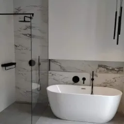Nowoczesna łazienka z wolnostojącą białą wanną, marmurowymi płytkami i czarną armaturą, oświetlona wiszącymi lampami.