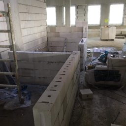 Globalneo Sp. z o.o. - Wnętrze w trakcie budowy z widocznymi ścianami z bloczków, narzędziami i butelką wody, ukazujące etap prac murarskich przed tynkowaniem.