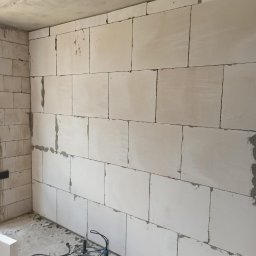 Globalneo Sp. z o.o. - Ściana z białych bloczków połączonych zaprawą, z widocznym miejscami ubytkiem zaprawy, na podłodze leży wiertarka udarowa.